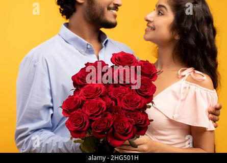 Romantisches Urlaubsdatum. Junge indische Ehepartner umarmen und halten Blumenstrauß, der sich gegenseitig anlächelt, aus der Nähe Stockfoto