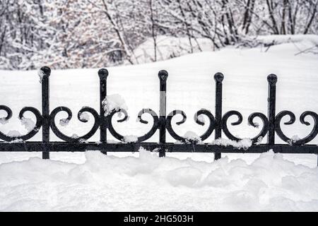 Schwarzes Metallgitter im Winter mit Schnee bedeckt. Schneefall- und Winterwetterkonzept. Stockfoto