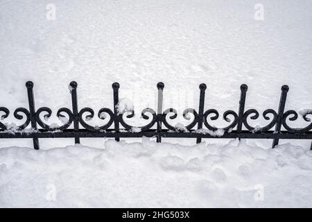 Schwarzes Metallgitter im Winter mit Schnee bedeckt. Schneefall- und Winterwetterkonzept. Stockfoto