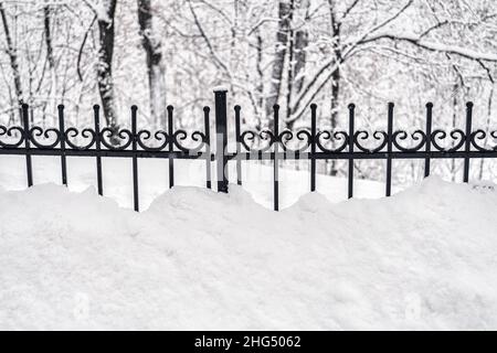 Schwarzes Metallgitter im Winter mit Schnee bedeckt. Schneefall- und Winterwetterkonzept. Stockfoto