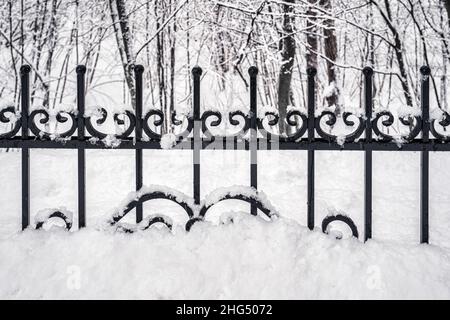 Schwarzes Metallgitter im Winter mit Schnee bedeckt. Schneefall- und Winterwetterkonzept. Stockfoto