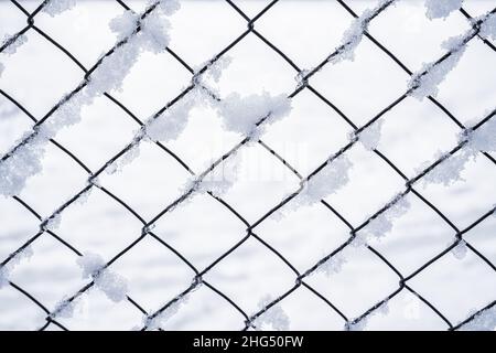 Schwarzes Metallgitter im Winter mit Schnee bedeckt. Schneefall- und Winterwetterkonzept. Stockfoto