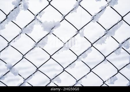 Schwarzes Metallgitter im Winter mit Schnee bedeckt. Schneefall- und Winterwetterkonzept. Stockfoto