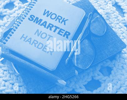 Stift, Brille und Spiralheft mit Work Smarter nicht härtere Wörter auf gehäkelter Stoffhintergrund. Karriere- und Geschäftskonzept Stockfoto