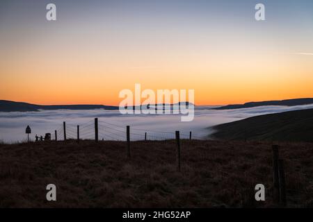 Ein Winter-HDR einer Wolkeninversion und eines Sonnenuntergangs vom Butter Tubs Pass mit Ingleborough in der Ferne, Wensleydale, Yorkshire, England. 14. Januar 2022 Stockfoto