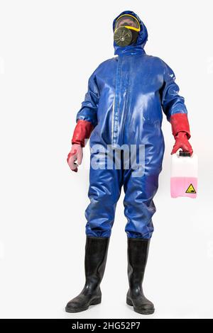 Mann in blauem Gummischutzanzug, mit Gasmaske, Gummihandschuhen und schwarzen Gummistiefeln hält einen Behälter mit Reinigungsflüssigkeit in der Hand. Stockfoto