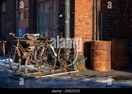 Rostige Fahrräder und Öltrommel gegen altes rotes Ziegelgebäude in der Nachmittagssonne auf dem alten Eisenbahnhof von Pasila, Helsinki, Finnland Stockfoto