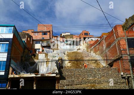 La Paz, Bolivien: Kommunale Arbeiter stabilisieren einen Hügel und beschädigte Häuser mit Käfigen gefüllt mit Felsen/Gabionen an einem Standort im Bezirk Tembladerani/Cotahuma. Unbefugte Ausgrabungen und Erdbewegungen durch einen der Grundstückseigentümer führten zum Einsturz eines Teils des Hügels. Viele von La Paz Hanggegenden wurden in instabilen Gebieten ohne entsprechende Genehmigungen oder Gebäudekontrollen gebaut. Senkungen und Erosion, die Erdrutsche und Einsturz von Häusern verursachen, sind häufig, besonders in der Regenzeit. Bei diesem Vorfall mussten 2 Häuser abgerissen werden, 6 weitere wurden stark betroffen. Stockfoto