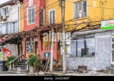 Verlassene Geschäfte und Häuser in einer armen Nachbarschaft in Südbulgarien, dem Balkan, Europa. Mehrfarbige Gebäude in schlechtem Zustand in einer Reihe. Stockfoto