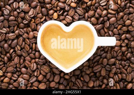 Kaffee in herzförmiger Tasse über Kaffeebohnen Hintergrund. Valentinstag-Konzept. Draufsicht, Platz für Text kopieren. Stockfoto