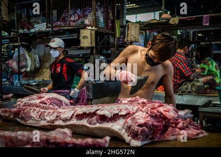 Bangkok, Thailand. 18th Januar 2022. Ein Arbeiter schlachtet Schweinefleisch, bevor es auf dem Markt verkauft wird.Arbeiter auf dem Großmarkt Bangkok Noi bereiten am 18. Januar 2022 frisch geschlachtetes Schweinefleisch zum Verkauf vor. Aufgrund von Lieferengpässen, Marktspekulationen und einem möglichen Ausbruch der Afrikanischen Schweinepest steigen die Schweinefleischkosten in Thailand in die Höhe, was den Preis für Grundnahrungsmittel in die Höhe schiessen lässt. Die schnelle Inflation hat zu einem plötzlichen landesweiten Anstieg von Lebensmitteln von der Straße bis zum Supermarkt geführt. Kredit: SOPA Images Limited/Alamy Live Nachrichten Stockfoto