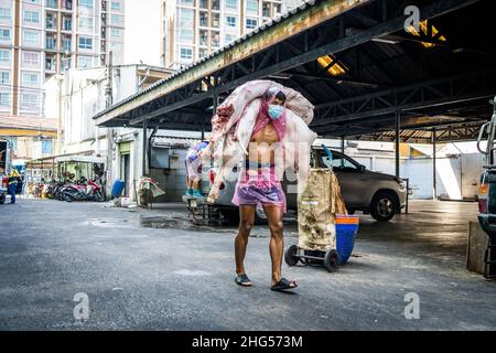 Bangkok, Thailand. 18th Januar 2022. Ein Arbeiter trägt Schweinekörper auf dem Rücken in einen Markt, auf dem sie geschlachtet und verkauft werden.Arbeiter auf dem Großmarkt Bangkok Noi bereiten am 18. Januar 2022 frisch geschlachtetes Schweinefleisch zum Verkauf vor. Aufgrund von Lieferengpässen, Marktspekulationen und einem möglichen Ausbruch der Afrikanischen Schweinepest steigen die Schweinefleischkosten in Thailand in die Höhe, was den Preis für Grundnahrungsmittel in die Höhe schiessen lässt. Die schnelle Inflation hat zu einem plötzlichen landesweiten Anstieg von Lebensmitteln von der Straße bis zum Supermarkt geführt. Kredit: SOPA Images Limited/Alamy Live Nachrichten Stockfoto