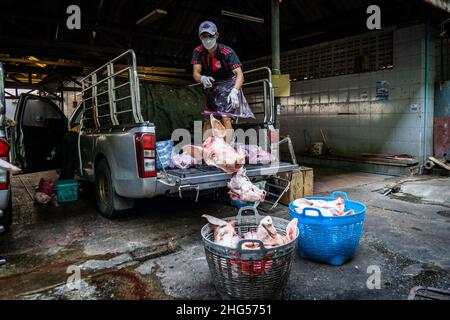 Bangkok, Thailand. 18th Januar 2022. Ein Arbeiter wirft Schweineköpfe in Sortierfächer, bevor sie auf dem Markt verkauft werden.Arbeiter auf dem Großmarkt Bangkok Noi bereiten am 18. Januar 2022 frisch geschlachtetes Schweinefleisch zum Verkauf vor. Aufgrund von Lieferengpässen, Marktspekulationen und einem möglichen Ausbruch der Afrikanischen Schweinepest steigen die Schweinefleischkosten in Thailand in die Höhe, was den Preis für Grundnahrungsmittel in die Höhe schiessen lässt. Die schnelle Inflation hat zu einem plötzlichen landesweiten Anstieg von Lebensmitteln von der Straße bis zum Supermarkt geführt. Kredit: SOPA Images Limited/Alamy Live Nachrichten Stockfoto