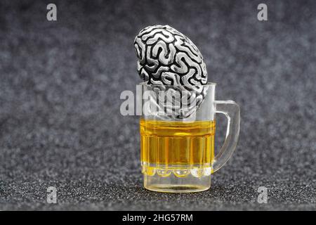 Anatomische Kopie eines menschlichen Gehirns in einem Miniatur-Bierkrug vor grauem Hintergrund. Alkohol und psychische Gesundheit Konzept. Stockfoto