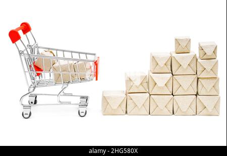 Miniatur-Einkaufswagen durch einen Stapel winziger Pappkartons, isoliert auf weißem Hintergrund. Liefer- und Paketdienstkonzept. Stockfoto