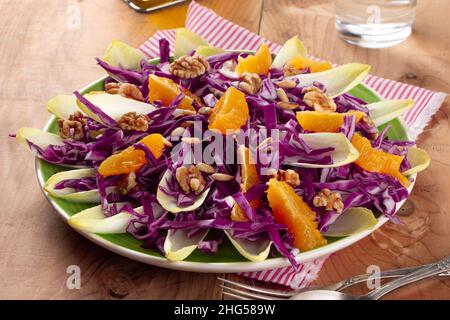 Rotkohlsalat mit Endive, Orangenfrüchten, gerösteten Pinienkernen und Walnüssen auf einem rustikalen Holztisch Stockfoto