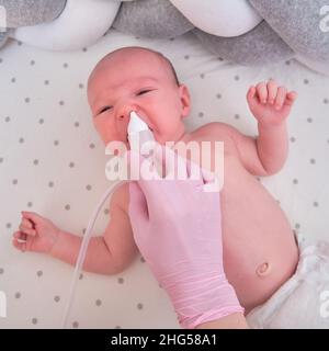 Der Arzt entfernt bei einem Neugeborenen eine laufende Nase mit einer Absaugvorrichtung. Krankenschwester in Uniform behandelt Kindernase für Grippe Stockfoto