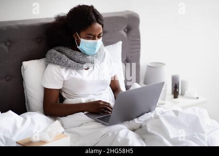 Kranke schwarze Frau in Gesichtsmaske Surfen im Internet Stockfoto