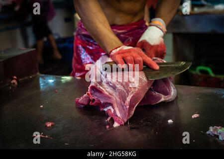 Bangkok, Thailand. 18th Januar 2022. Ein Arbeiter schlachtet Schweinefleisch, bevor es auf dem Markt verkauft wird.Arbeiter auf dem Großmarkt Bangkok Noi bereiten am 18. Januar 2022 frisch geschlachtetes Schweinefleisch zum Verkauf vor. Aufgrund von Lieferengpässen, Marktspekulationen und einem möglichen Ausbruch der Afrikanischen Schweinepest steigen die Schweinefleischkosten in Thailand in die Höhe, was den Preis für Grundnahrungsmittel in die Höhe schiessen lässt. Die schnelle Inflation hat zu einem plötzlichen landesweiten Anstieg von Lebensmitteln von der Straße bis zum Supermarkt geführt. (Foto von Matt Hunt/SOPA Images/Sipa USA) Quelle: SIPA USA/Alamy Live News Stockfoto