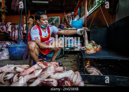 Bangkok, Thailand. 18th Januar 2022. Arbeiter brüten Schweinebeine, bevor sie auf dem Markt verkauft werden. Arbeiter auf dem Großmarkt Bangkok Noi bereiten am 18. Januar 2022 frisch geschlachtetes Schweinefleisch zum Verkauf vor. Aufgrund von Lieferengpässen, Marktspekulationen und einem möglichen Ausbruch der Afrikanischen Schweinepest steigen die Schweinefleischkosten in Thailand in die Höhe, was den Preis für Grundnahrungsmittel in die Höhe schiessen lässt. Die schnelle Inflation hat zu einem plötzlichen landesweiten Anstieg von Lebensmitteln von der Straße bis zum Supermarkt geführt. (Foto von Matt Hunt/SOPA Images/Sipa USA) Quelle: SIPA USA/Alamy Live News Stockfoto
