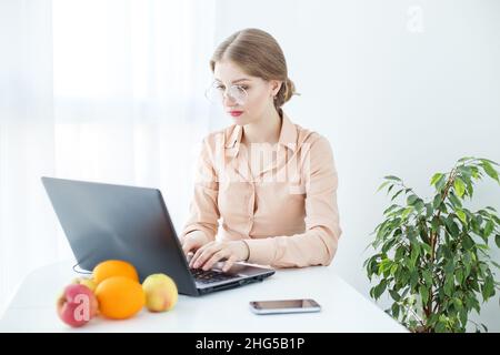 Frau mit Brille in beigefarbener Bluse. Studentin nutzt Laptop und Internet im Studium. Stockfoto