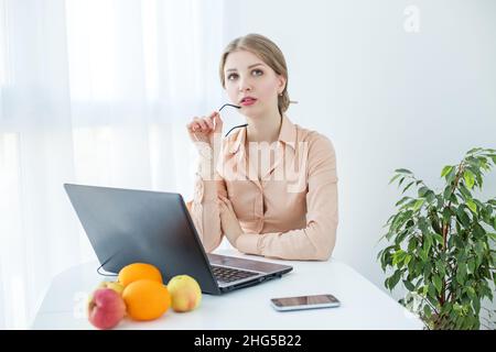 Frau mit Brille in beigefarbener Bluse. Studentin nutzt Laptop und Internet im Studium. Stockfoto