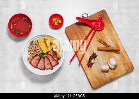 Sarawak Noodle Dry and Soup, Sarawak Mee Tai Bak und Sarawak Kway Teow in weißer Schüssel Draufsicht mit rohem Knoblauch, Löffel und Essstäbchen auf Holzschnitt Stockfoto