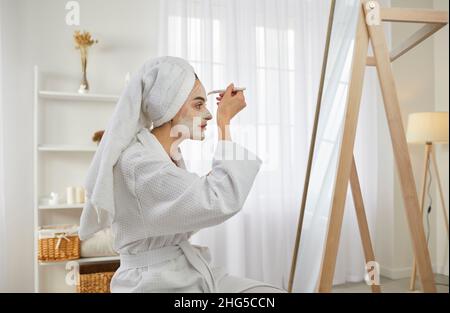 Schöne junge Frau am Morgen nach der Dusche trägt feuchtigkeitsspendende kosmetische Maske auf ihr Gesicht. Stockfoto