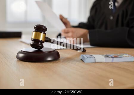 Nahaufnahme des Richters Gavel stehen auf Schallblock und Geldbündel auf dem Tisch auf dem Hintergrund des Menschen. Stockfoto