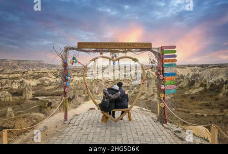 Goreme, Türkei. Ein verliebtes Paar sitzt auf einer herzförmigen Bank auf dem Hintergrund von Feenkaminen im Love Valley, Felsformationen in Kappadokien Stockfoto