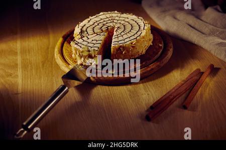 Esterhazys Mandelschokoladenkuchen mit einem abgeschnittenen Stück und einem Spachtel liegt auf einem Brett mit einem Holztisch im Hintergrund. Stockfoto