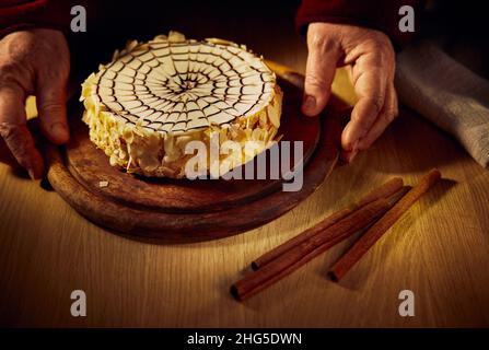 Eine Frau hält ein Brett mit Esterhazy Mandel-Schokoladenkuchen in den Händen vor dem Hintergrund eines Holztisches. Stockfoto