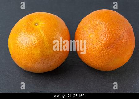 Nahaufnahme von zwei ganzen Grapefruits isoliert auf schwarzem Schneidebrett. Stockfoto