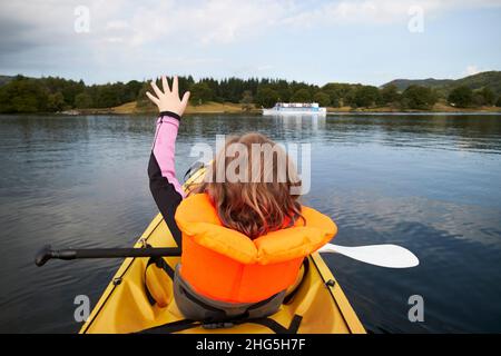 Ein junges, siebenjähriges Mädchen, das eine Rettungsweste vor einem zweiköpfigen Kajak trägt, fährt mit der Fähre über windermere im Sommer Lake District, cumbria, Stockfoto