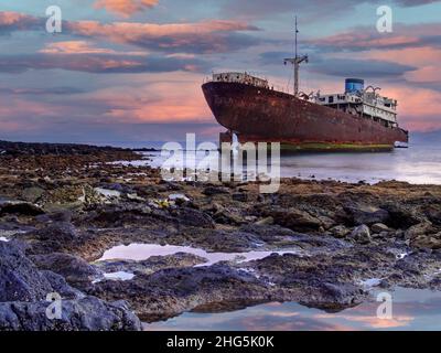 Rostiges Schiffswrack liegt in einer Bucht mit flachem Wasser bei Sonnenuntergang auf den Kanarischen Inseln von Lanzarote, Spanien Stockfoto