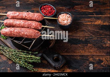 Rohe Kofta- oder lula-Kebabs-Spieße auf einem Grill mit Kräutern. Dunkler Holzhintergrund. Draufsicht. Speicherplatz kopieren Stockfoto