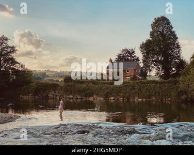 Teenager-Mädchen, die in der Dämmerung Steine auf dem Fluss Wye abschaufeln Stockfoto