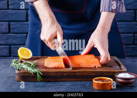 Der Mensch schneidet Lachsfilet. Der Koch schneidet ein Fischfilet auf einem rustikalen Holzbrett in einer Restaurantküche aus nächster Nähe Stockfoto