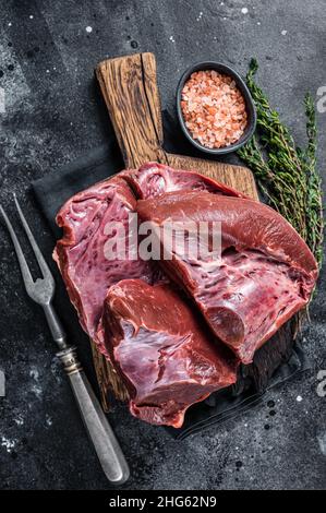 Rohes geschnittes Rind- oder Kalbsherz auf einem Schlachtbrett. Schwarzer Hintergrund. Draufsicht Stockfoto