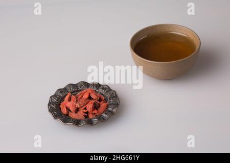 Traditionelle orientalische Tonerbecherschale mit frisch gebrühtem schwarzem Tee. Rote Goji-Beeren auf einer Untertasse. Stockfoto
