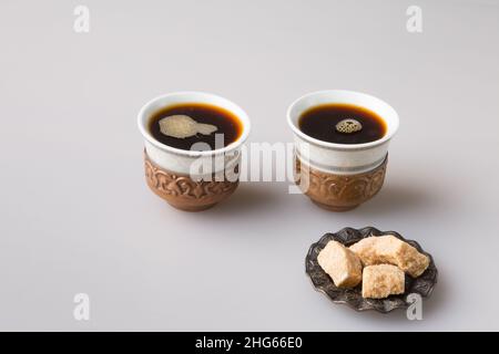 Zwei traditionelle Kaffeetassen werden mit frisch gebrühtem türkischen Kaffee gefüllt. Gepresster brauner Zucker auf einer Untertasse. Das Konzept des Minimalismus. Stockfoto