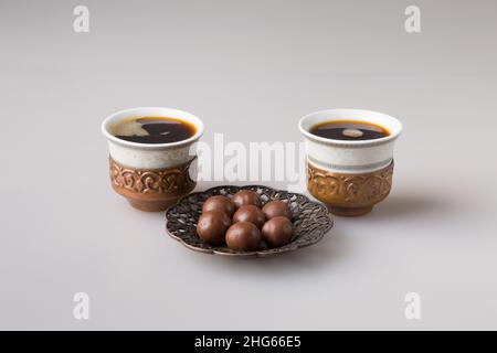 Zwei traditionelle Kaffeetassen werden mit frisch gebrühtem türkischen Kaffee gefüllt. Milchschokoladenkugeln auf einer Untertasse. Das Konzept des Minimalismus. Stockfoto