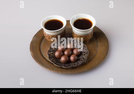 Zwei traditionelle Kaffeetassen werden mit frisch gebrühtem türkischen Kaffee gefüllt. Milchschokoladenkugeln auf einer Untertasse. Das Konzept des Minimalismus. Stockfoto