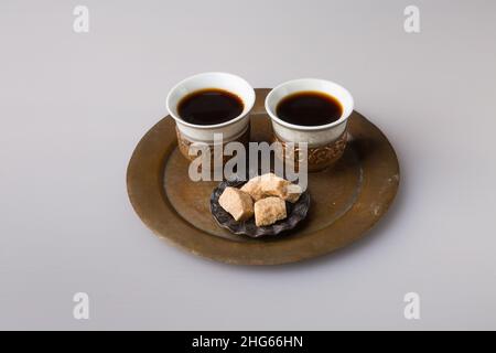 Zwei traditionelle Kaffeetassen werden mit frisch gebrühtem türkischen Kaffee gefüllt. Gepresster brauner Zucker auf einer Untertasse. Das Konzept des Minimalismus. Stockfoto
