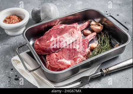 Rohe Tomahawk Kalbssteaks in Stahlblech mit Kräutern. Grauer Hintergrund. Draufsicht Stockfoto