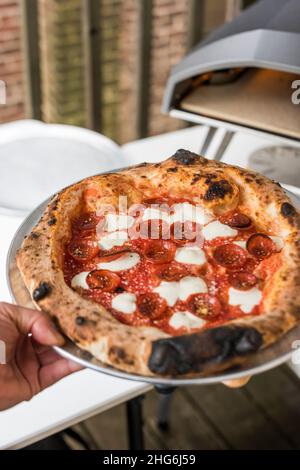 Pizzaiolo mit frischem Pfefferoni-Kuchen, der im Pizzaofen im Freien zubereitet wird Stockfoto