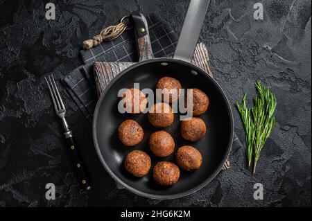 Gebratene Fleischbällchen auf pflanzlicher Basis in einer Pfanne mit Kräutern. Schwarzer Hintergrund. Draufsicht Stockfoto