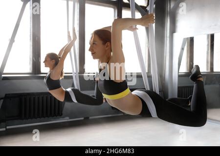 Zwei junge Frauen, die fliegen Yoga-Übung für das Stretching tun, das auf Riemen oder Hängematte in der Turnhalle hängt Stockfoto