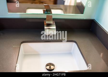 Neuer moderner, stilvoller, zeitgenössischer Wasserhahn in der Nähe des Badezimmers mit Chromgriff aus Edelstahl und weißem Waschbecken mit Spiegelreflexion im Haus Stockfoto