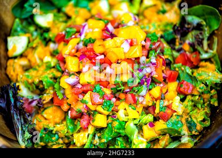 Nahaufnahme-Makro des Salats in einer Schüssel mit rotem Blattsalat, Tomaten und gehackten, geschnittenen Mangosalsazwiebeln, Dressing mit Koriander, oben flach Stockfoto